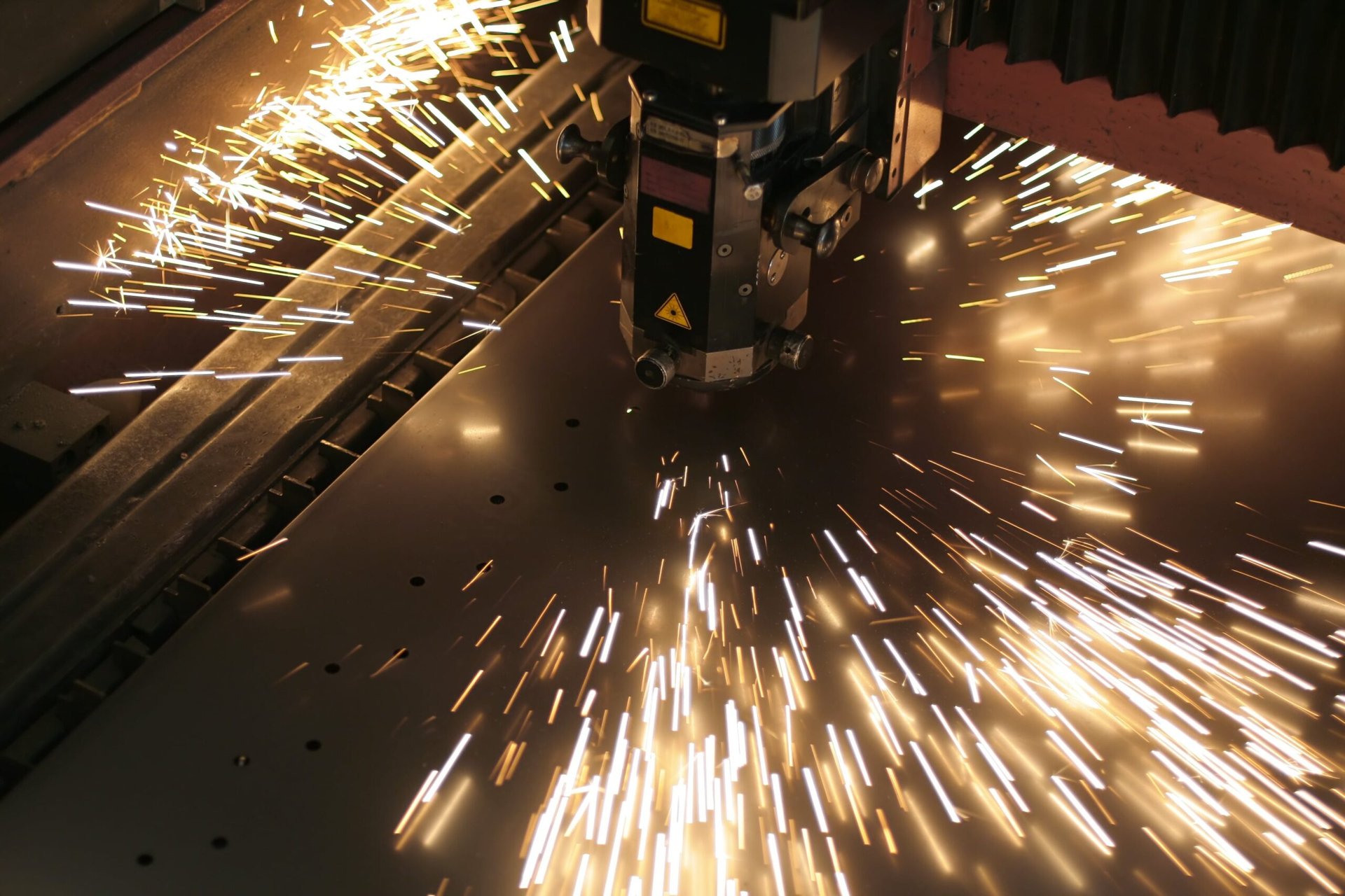 Laser cutting head sending sparks across sheet metal